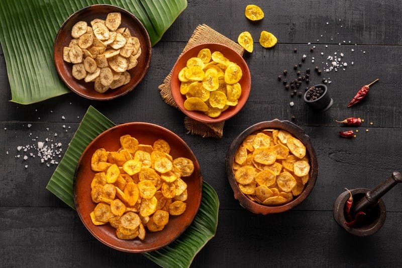Overhead food photograph of plated sweets on a dark table with banana leaves